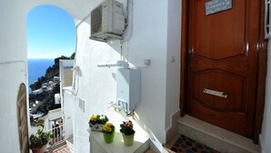 A balcony with a view of the sea, a wooden door with a 'home sweet home' sign, and a small table with potted plants. - Casa Carola beautiful sea view and relax !!!! (Positano)