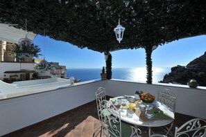 A terrace with a table set for dining, overlooking a coastal view.