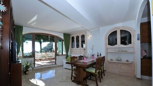 A dining area with a wooden table and chairs, a large window with a view, and a cabinet with decorative items. - Casa Carola beautiful sea view and relax !!!! (Positano)