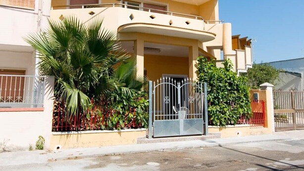 A two-story residential building with a curved balcony, a gated entrance, and a small garden with palm trees. - TORRE LAPILLO P. LAND 2 APARTMENTS 100 MT FROM THE SEA, ON THE MAIN COURSE (Torre Lapillo)