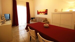 A dining area with a red table, white chairs, a sofa, and a cabinet. - TORRE LAPILLO P. LAND 2 APARTMENTS 100 MT FROM THE SEA, ON THE MAIN COURSE (Torre Lapillo)