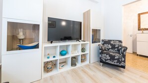 A modern living room with a flat-screen TV on a white stand, a patterned armchair, and a shelf with decorative items. - Fresh and Clean apt for 6 in Koukaki (Athens)