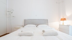A hotel room with a bed, two pillows, a nightstand, a lamp, and a wall sign with city names. - Fresh and Clean apt for 6 in Koukaki (Athens)