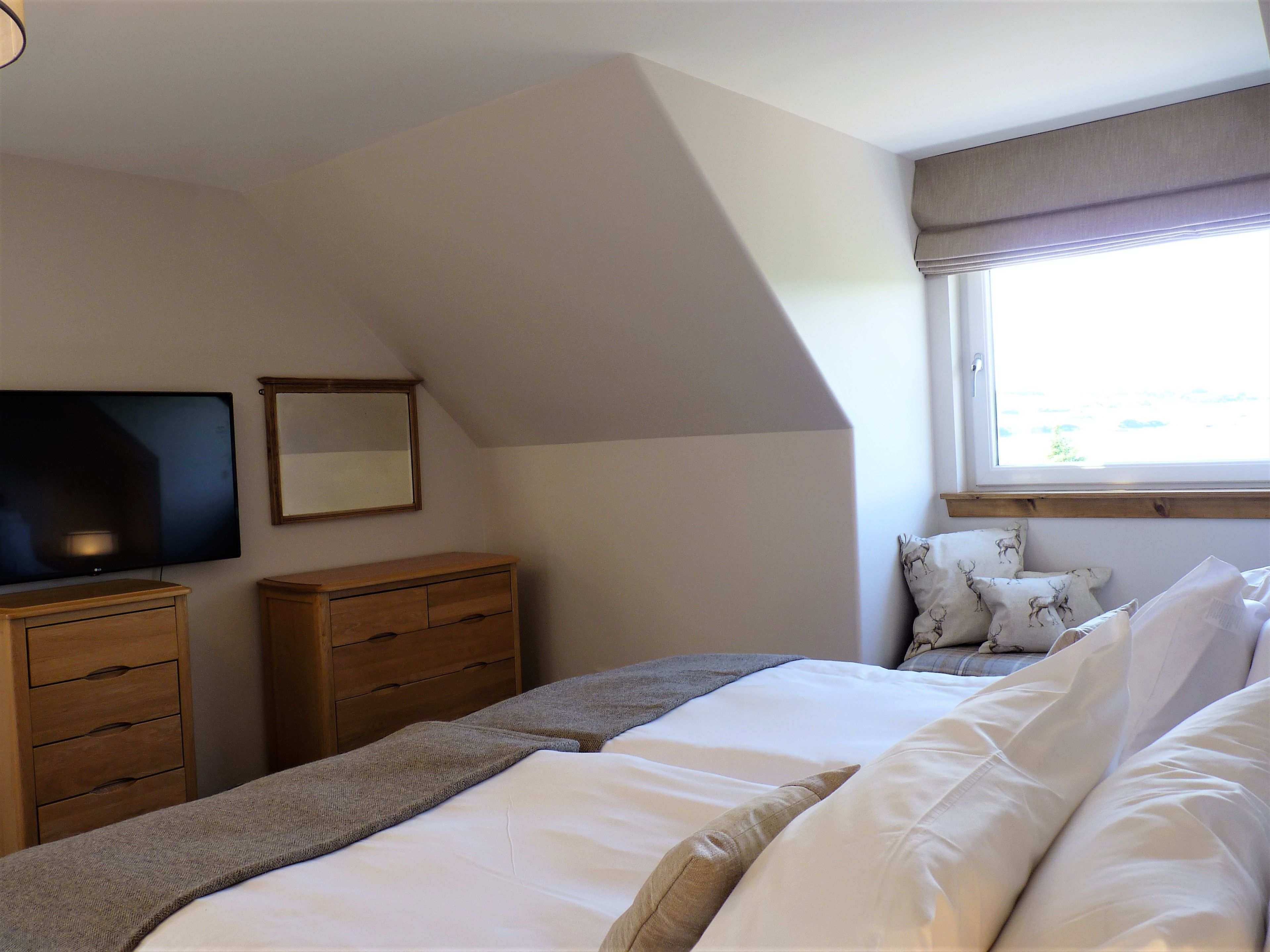 A bedroom with a bed, a dresser, a television, and a window with curtains.