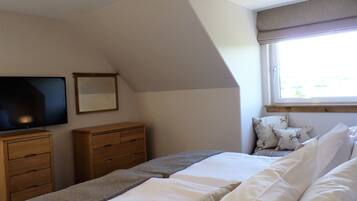 A bedroom with a bed, a dresser, a television, and a window with curtains.