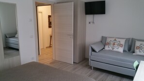 A modern, minimalistic room with a grey sofa, patterned cushions, a flat-screen TV mounted on the wall, and a wooden wardrobe. - Il Sole e la Luna B&B in Garda (Garda)