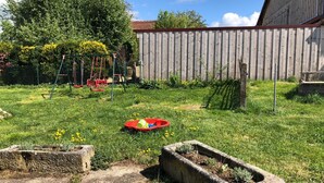 Ein Garten mit Schaukeln, einer roten Spielanlage und einem Betonpflanzbehälter mit Pflanzen.