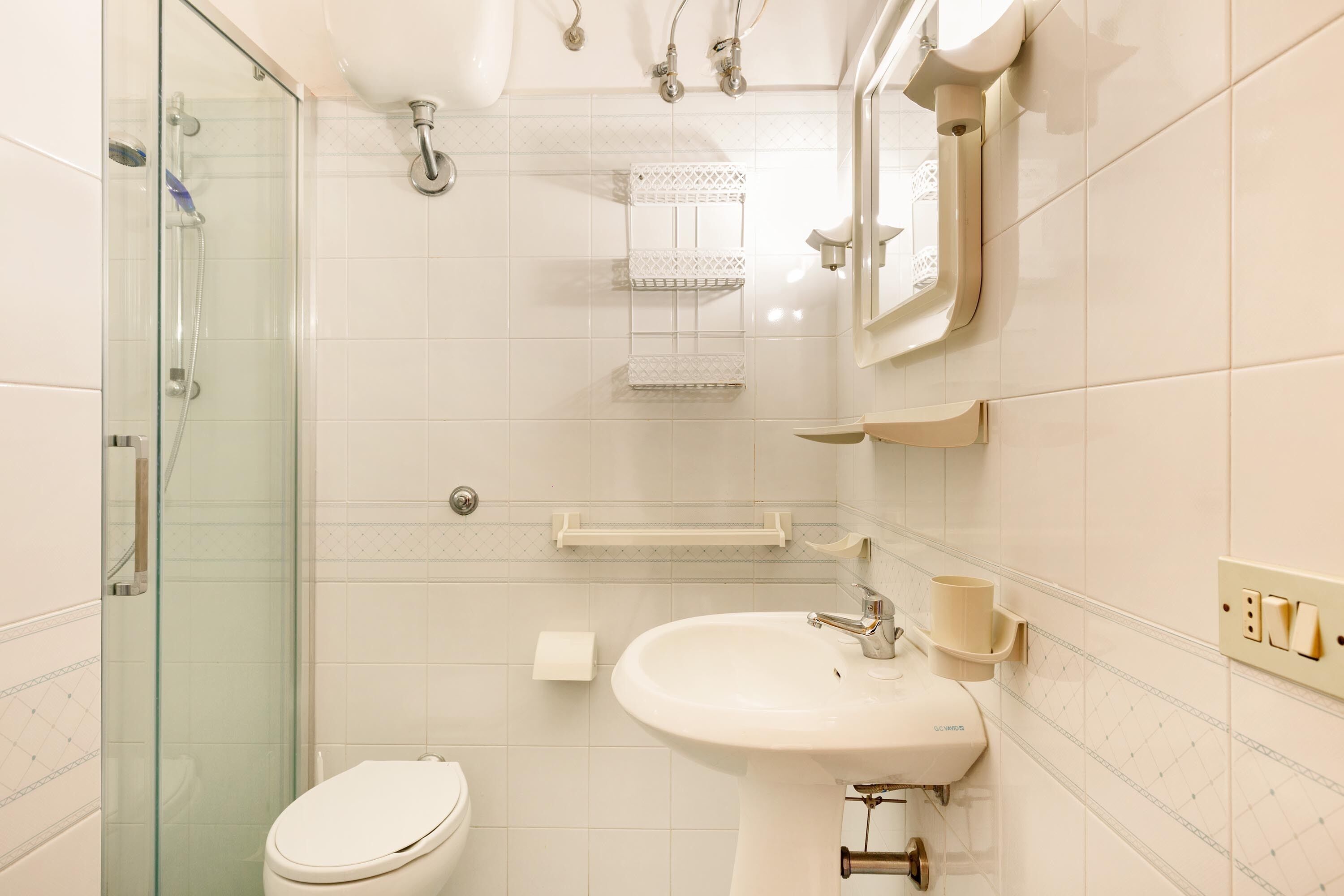 A bathroom with a glass shower enclosure, a toilet, a sink with a mirror, and a towel rack.
