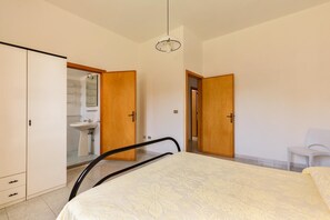 Ein Schlafzimmer mit Bett, Kleiderschrank, Stuhl und einem durchgehenden Türrahmen sichtbarem Badezimmer.