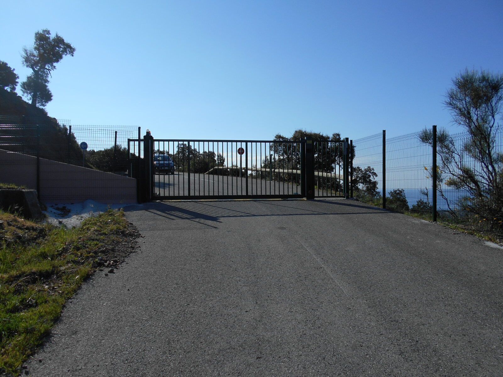 A gated entrance with a metal gate, a paved path, and a fence.
