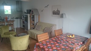 Een knus woongedeelte met een kitchenette, een bank, een eettafel met een tafelkleed met bloemenmotief, en een stoel.