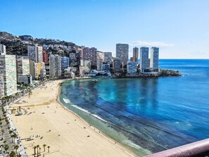A coastal cityscape with a wide sandy beach, high-rise buildings, and a clear blue sea.
