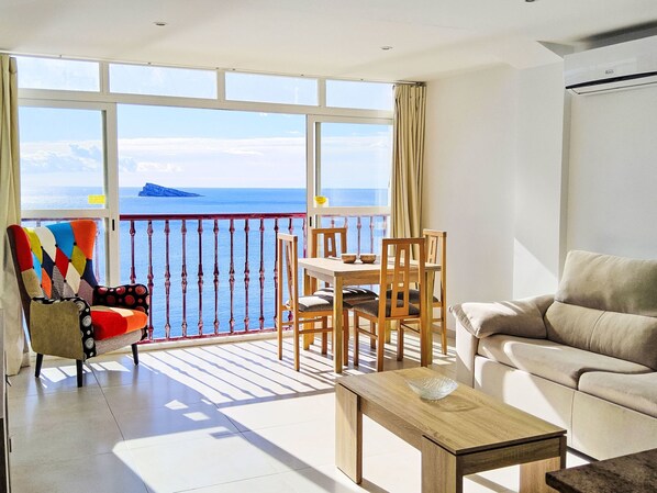 A balcony with a view of the sea, a dining table with chairs, a sofa, and a colorful armchair.