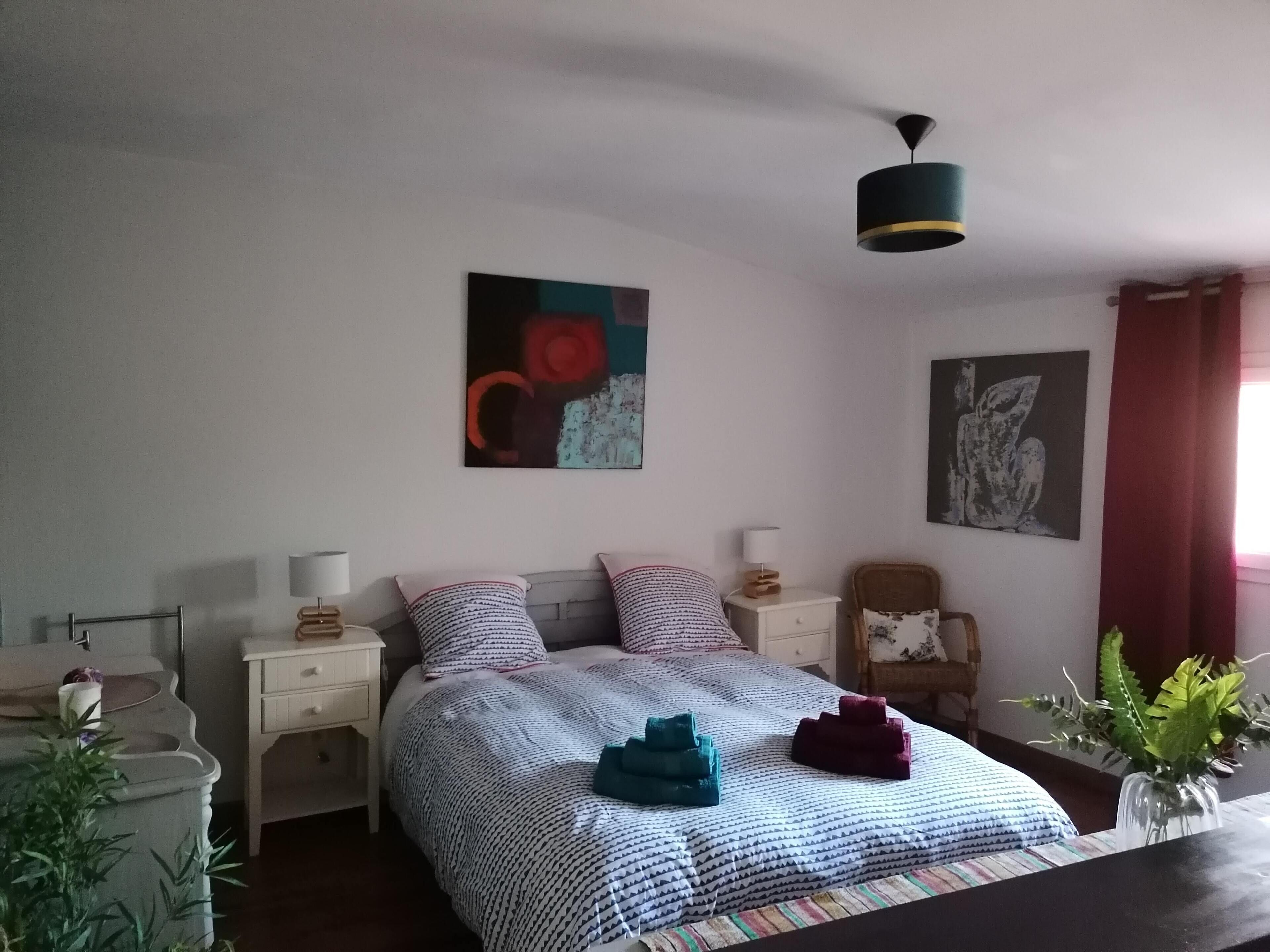 A bedroom with a bed, nightstands, a chair, and artwork on the walls.