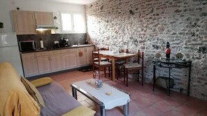 Un accogliente soggiorno con divano e tavolino, una cucina con mobili in legno e una parete in pietra, e un'area pranzo con tavolo e sedie.