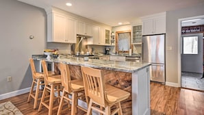 A modern kitchen with a large island, wooden bar stools, and stainless steel appliances. - Updated Condo Next to Burke Mountain Bike Trails! (East Burke)