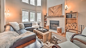A spacious living room with a fireplace, leather sofas, and a large window overlooking a snowy landscape. - Updated Condo Next to Burke Mountain Bike Trails! (East Burke)