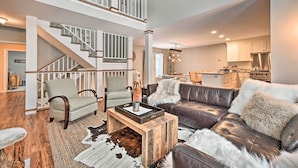 A spacious living area with a high ceiling, a staircase, a leather sofa, and a dining area. - Updated Condo Next to Burke Mountain Bike Trails! (East Burke)