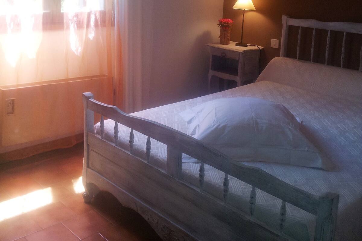 A bedroom with a bed, a nightstand, a lamp, and a window with curtains.