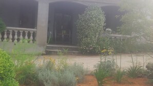 Een gebouw met een pannendak, een overdekte veranda en een tuin met verschillende planten en bloemen.