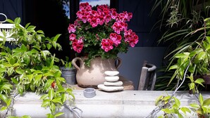 Een stenen tafel met een vaas roze bloemen, omringd door groene planten.