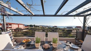 Eine Terrasse mit Frühstückstisch, Topfpflanzen und Blick auf das Meer und die Gebäude.