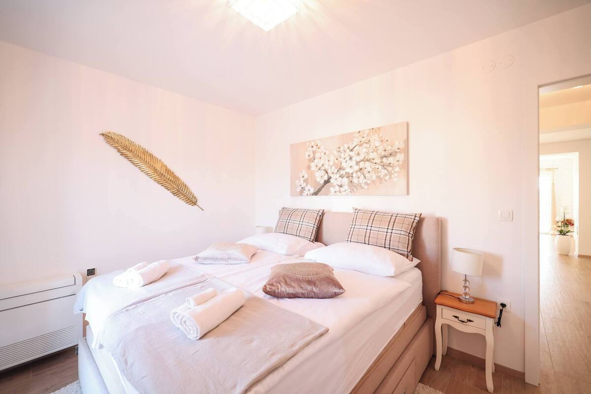 A bedroom with a large bed, a bedside table with a lamp, and a wall-mounted artwork.