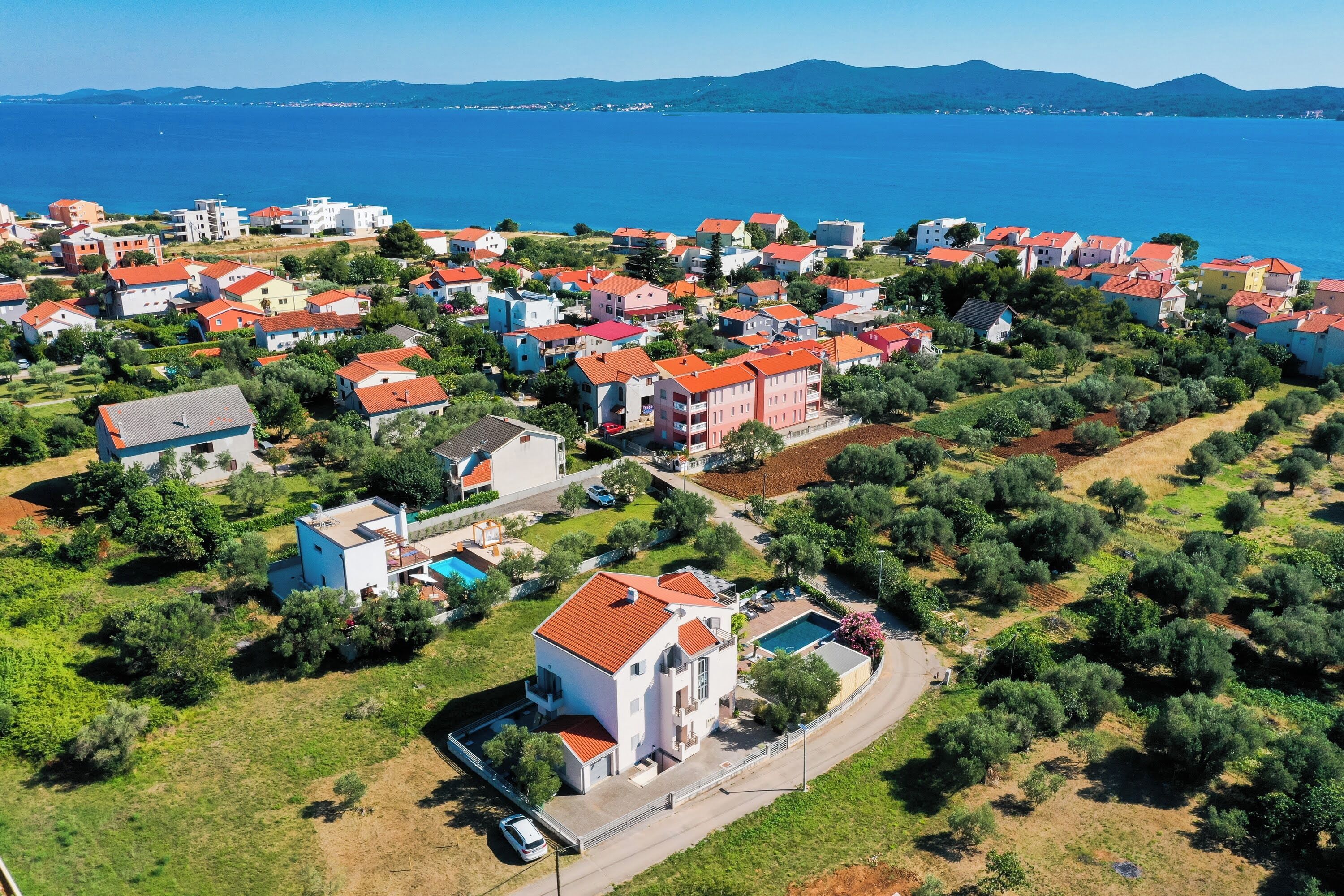 Vista aérea de una zona residencial costera con casas, una piscina y una carretera.