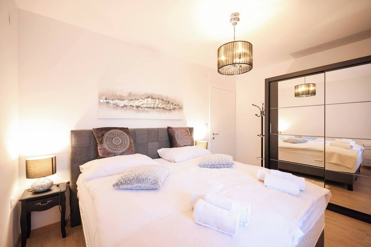A neatly made bed with white linens and pillows, a bedside lamp, and a wall-mounted artwork above the bed.