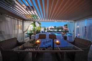 An outdoor dining area with a glass table, wicker chairs, and candles.