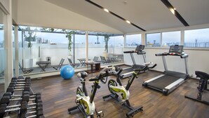 A gym with exercise equipment, large windows, and a view of the city.