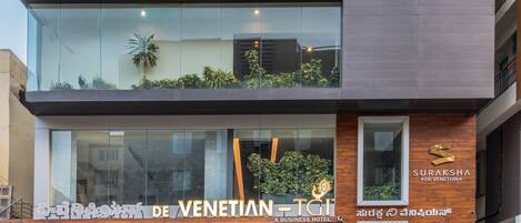 Un hotel de varios pisos con un diseño moderno, con balcones adornados con plantas, amplias ventanas y un cartel que indica que es un hotel para negocios.