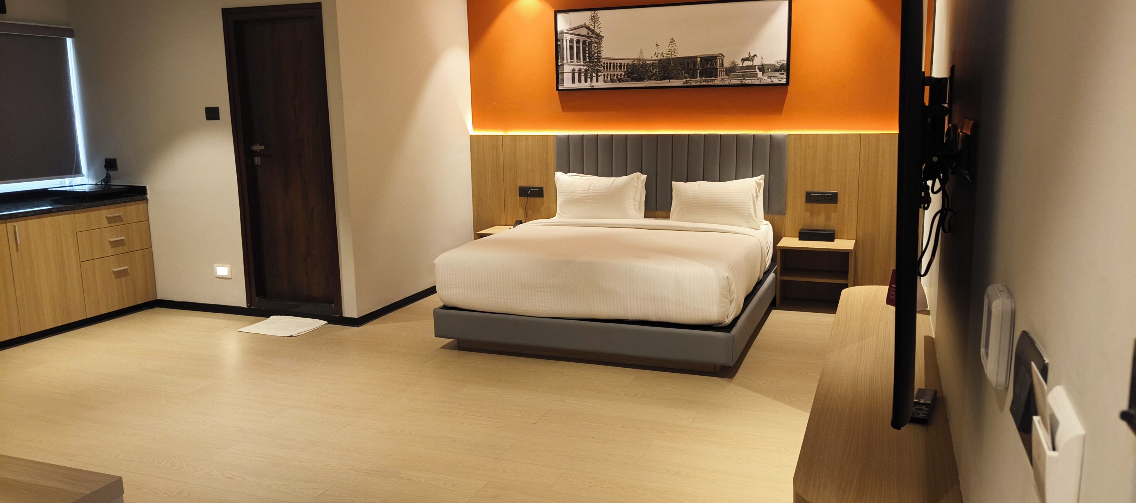 A modern hotel room with a bed, bedside tables, a flat-screen TV, and a framed picture on the wall.