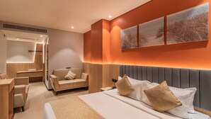 A modern hotel room with a bed, a sofa, a desk, and a mirror.