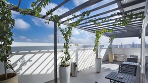 A rooftop terrace with potted plants, outdoor seating, and a city view.