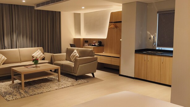 A modern living room with a sofa, armchair, and coffee table. There is a kitchen area with a countertop and cabinets.