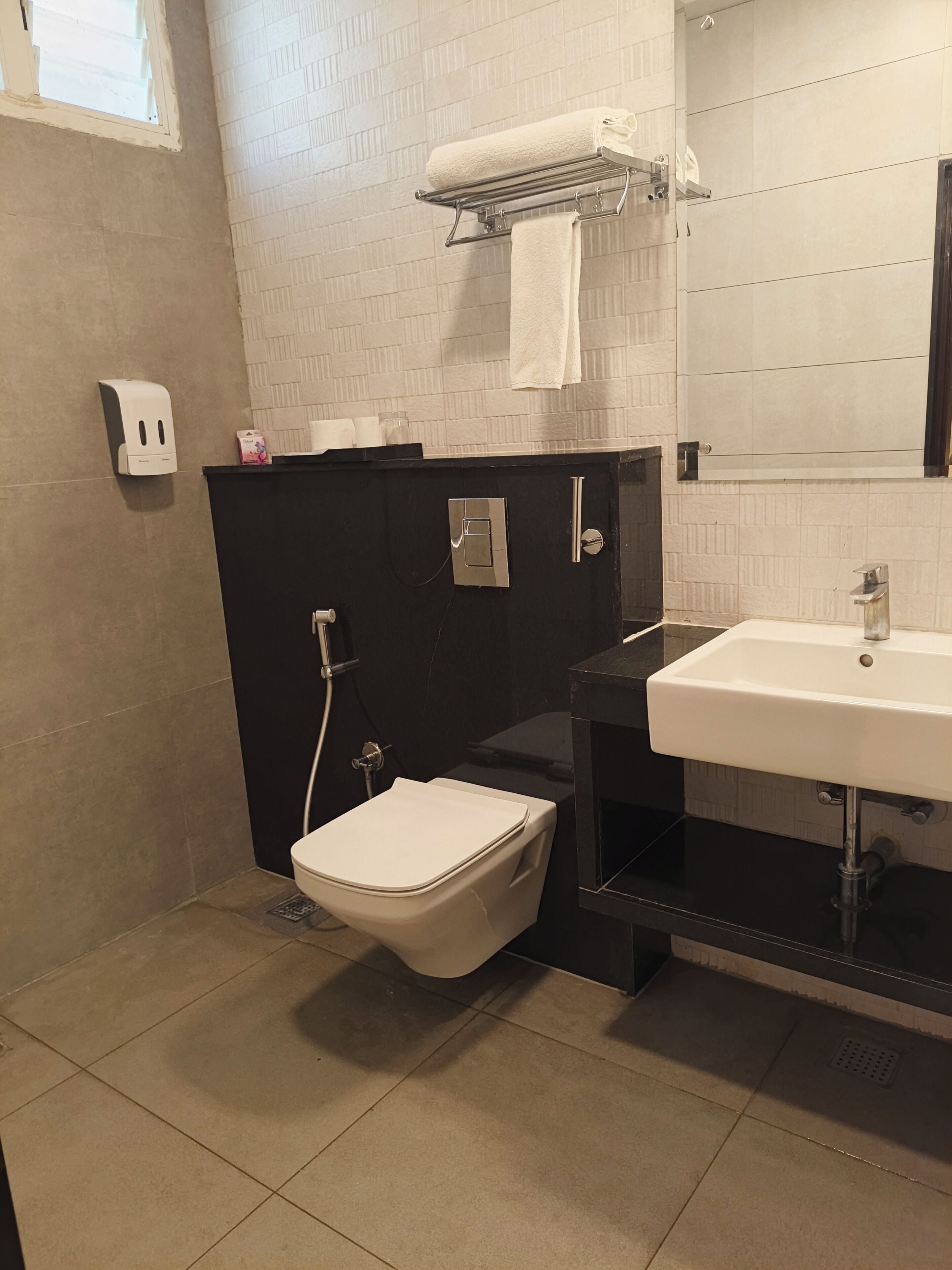 A bathroom with a toilet, sink, towel rack, and a soap dispenser.