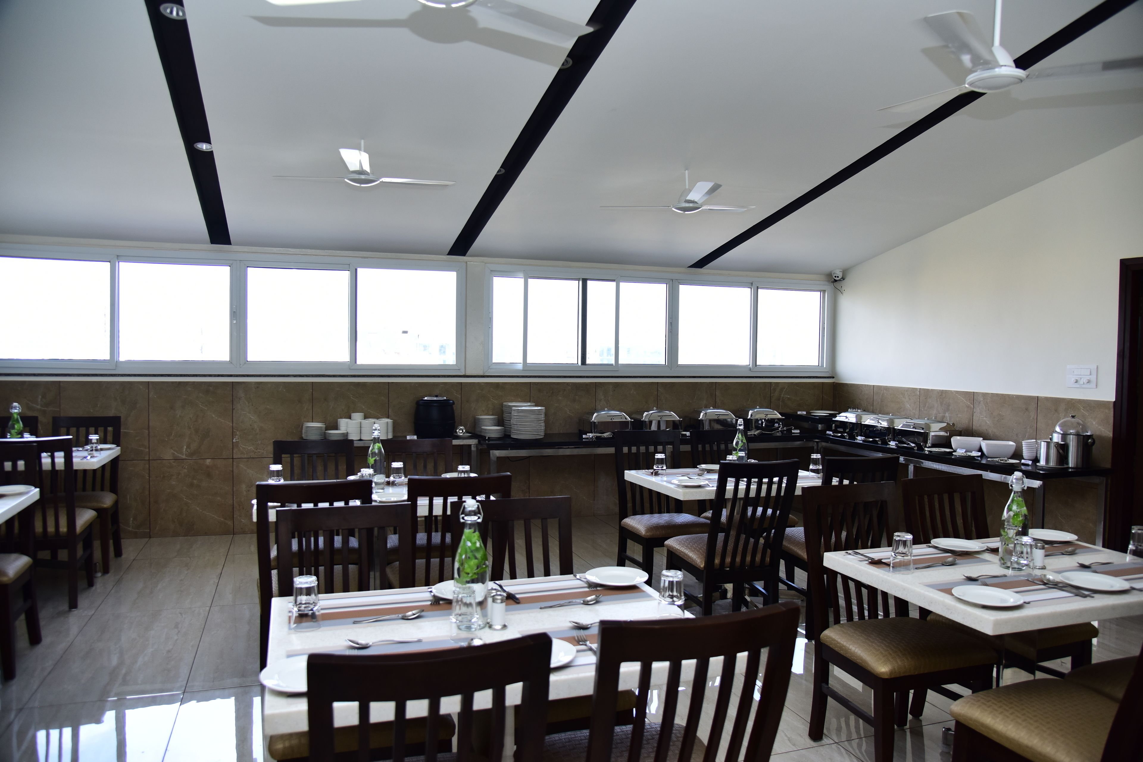 A restaurant with multiple dining tables and chairs, large windows, and ceiling fans.