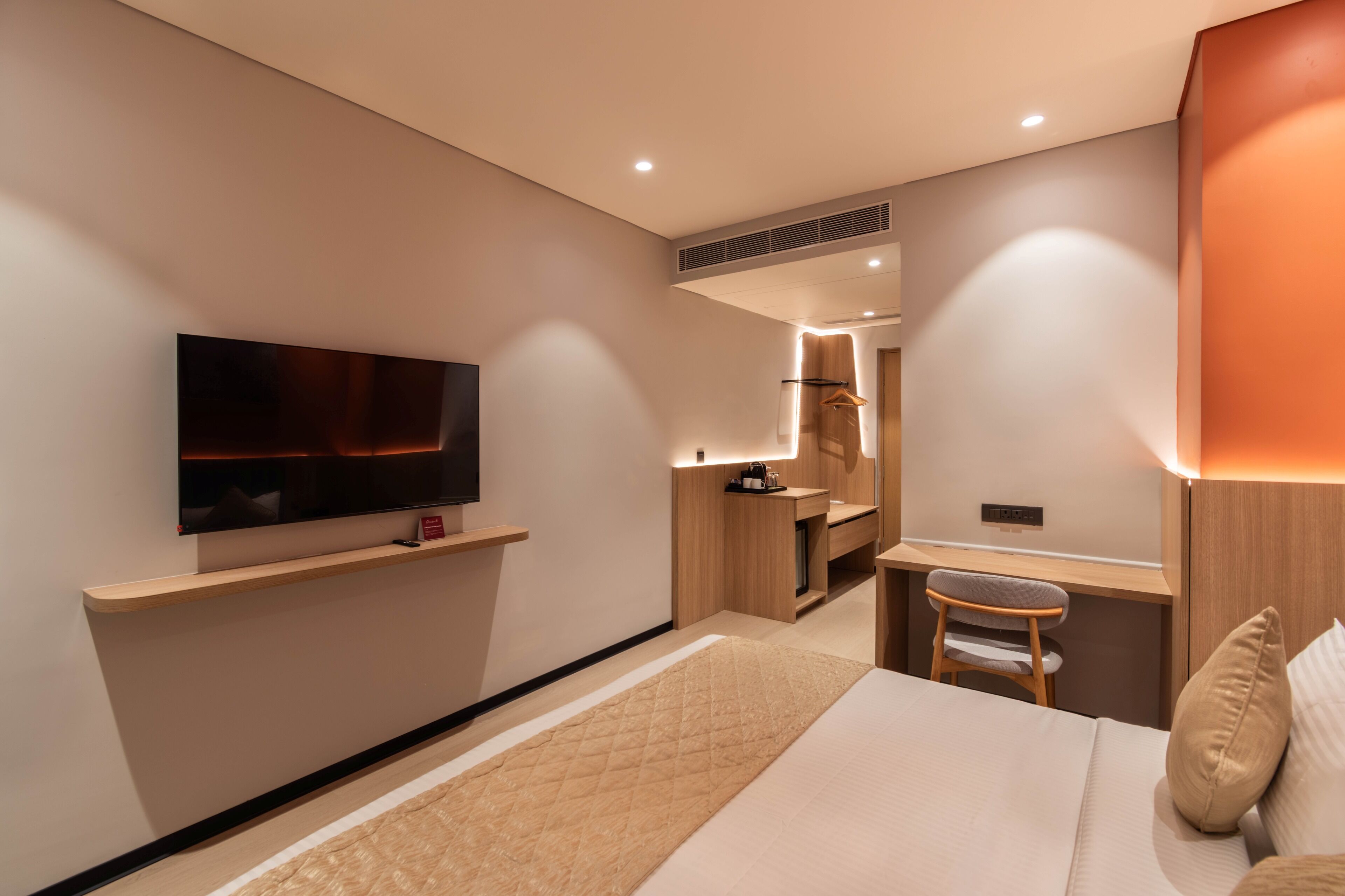 Ein modernes Hotelzimmer mit Flachbildfernseher, Schreibtisch, Stuhl, Bett und Spiegel.