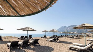 A beach with sun loungers and umbrellas, a clear sky, and mountains in the background.