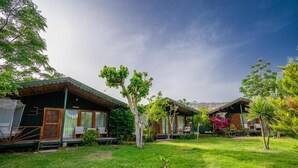 A row of cabins with a grassy lawn and trees, each with a porch and a window.
