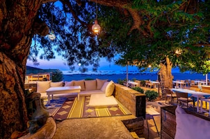 Un espacio al aire libre acogedor con vistas al mar, amueblado con cojines y mesas, y decorado con luces colgantes.
