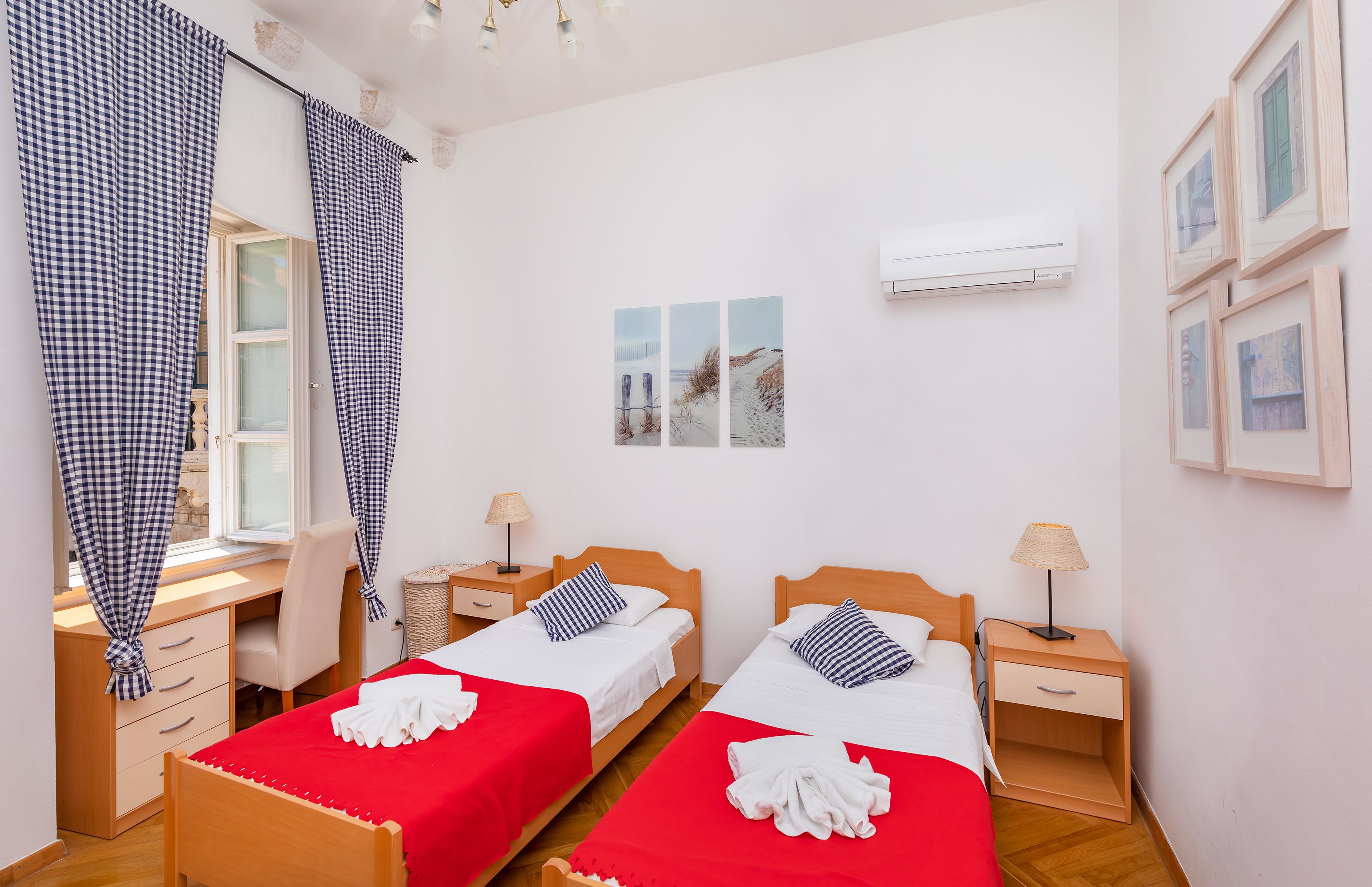 A bedroom with two beds, a desk, and a chair. There are two bedside tables with lamps.