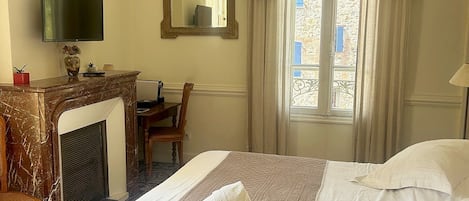 Habitación de hotel con cama, escritorio, televisor, chimenea y ventana con cortinas.