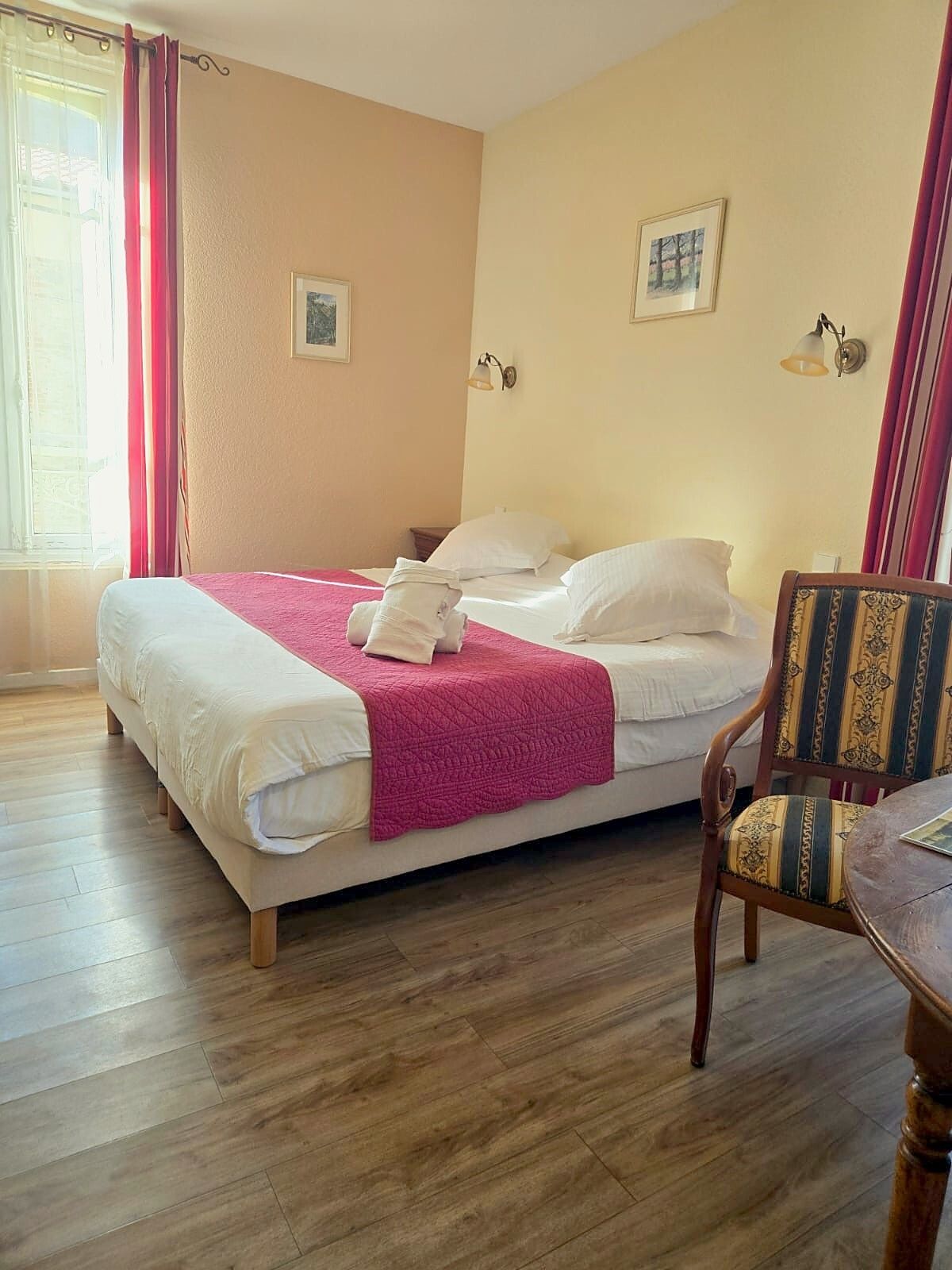 Une chambre d’hôtel avec un lit, une chaise, une fenêtre avec des rideaux et deux lampes fixées au mur.