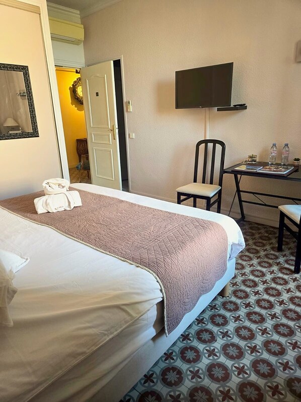 Une chambre d’hôtel avec un lit, un bureau et une chaise, une télévision et un sol à motifs.