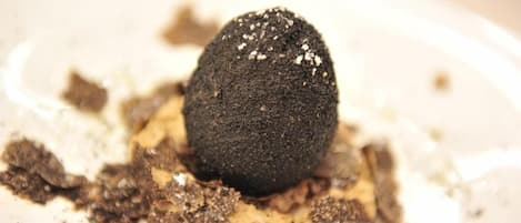 Un postre con una esfera oscura sobre un plato blanco, rodeado de virutas de chocolate.
