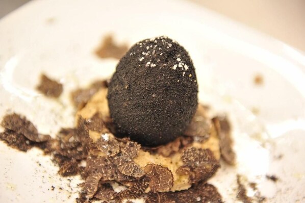 A dessert with a dark sphere on a white plate, surrounded by chocolate shavings. - Auberge du Cellier (Montner)