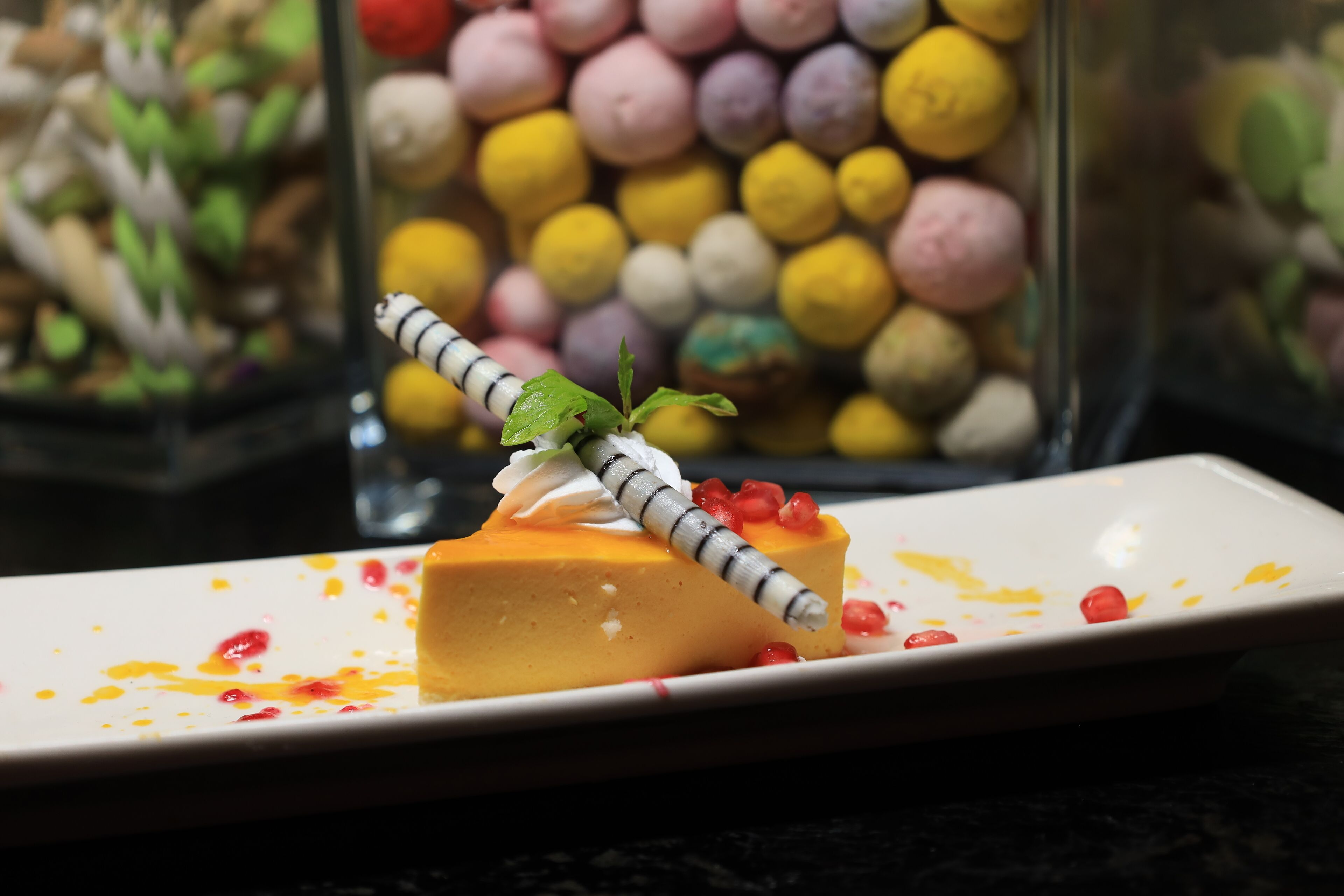 Un dessert su un piatto bianco, decorato con guarnizione a righe e semi di melograno, con un fondo di coloratissimi macaron.
