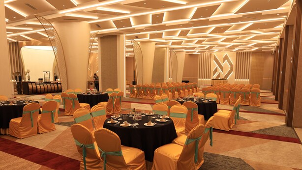 A conference room with round tables, chairs, and a stage area. - The Aananda Imperial (Bilaspur)